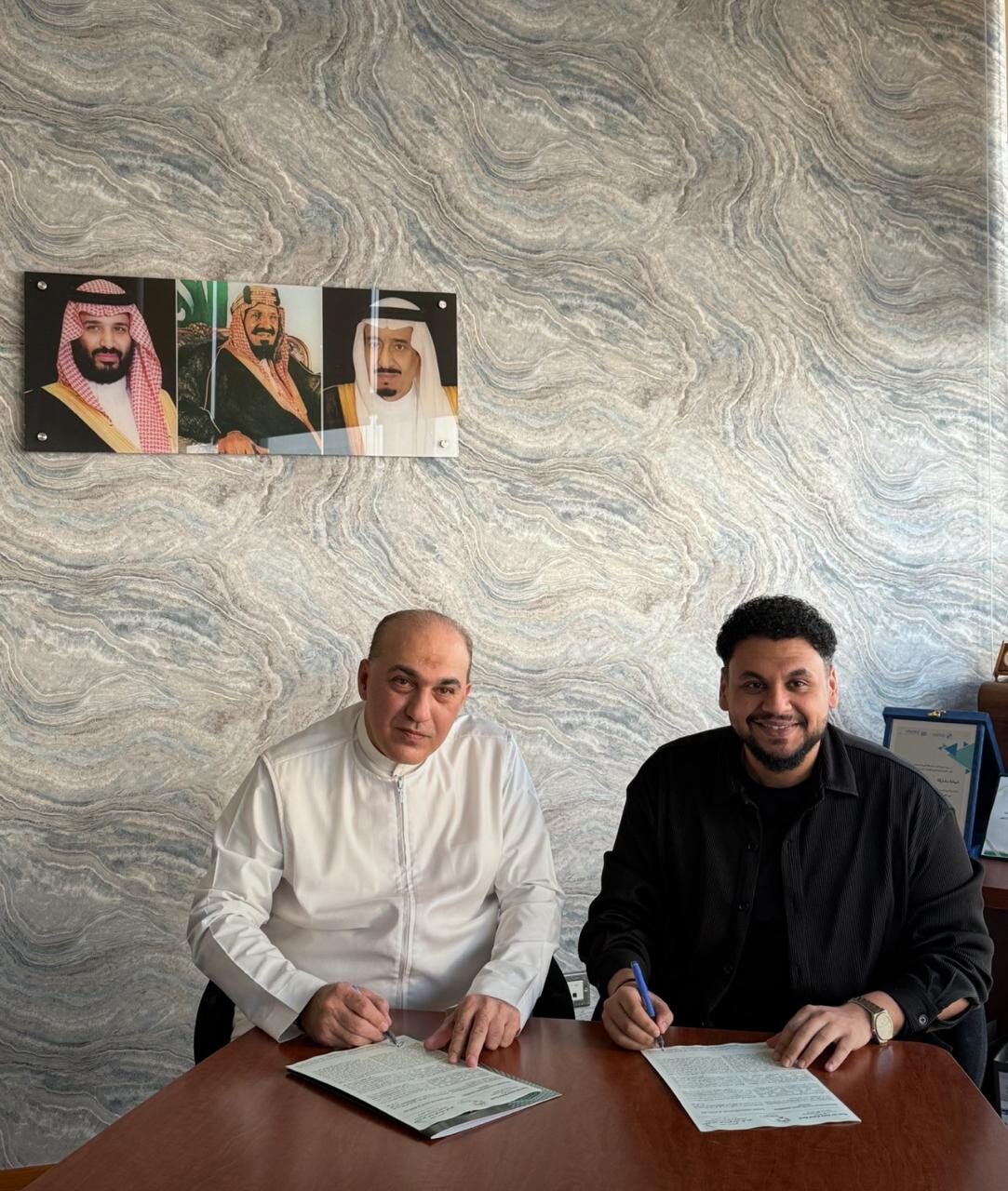 Mazin Kurdi and the artist Mohamed Abu Al-Enein signing an agreement at the office.